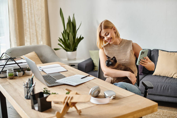Kobieta z krótkimi włosami siedzi na kanapie, delikatnie trzymając kota w ramionach, tworząc spokojną i harmonijną atmosferę. - Zdjęcie, obraz