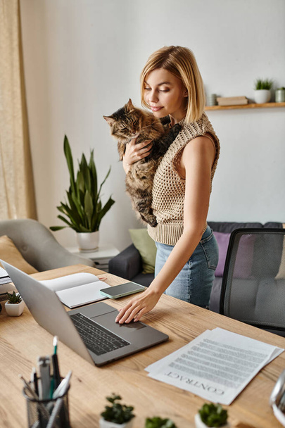 Kobieta z krótkimi włosami przytula kota podczas korzystania z laptopa w przytulnym domu. - Zdjęcie, obraz