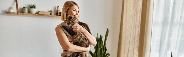 Een vrouw staat gracieus voor een raam, vredig haar kat in een tedere omhelzing vasthoudend. - Foto, afbeelding
