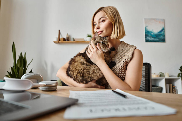 Una donna attraente con i capelli corti si siede a una scrivania, tenendo e accarezzando il suo gatto contenuto in un ambiente interno accogliente. - Foto, immagini