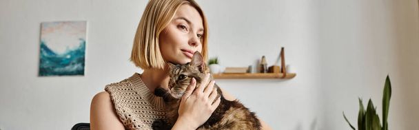 Egy rövid hajú nő szeretettel tartja a macskáját a kezében, összebarátkozva és megosztva egy különleges pillanatot otthon.. - Fotó, kép