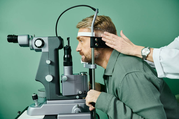 Ο σκληρά εργαζόμενος γιατρός εξετάζει τα μάτια ατόμων μέσω ενός μικροσκοπίου σε ένα γραφείο γιατρών για τη διόρθωση όρασης λέιζερ. - Φωτογραφία, εικόνα