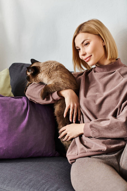 Kobieta z krótkimi włosami relaksuje się na kanapie, ciesząc się doskonałym czasem spędzonym z towarzyszką kotów. - Zdjęcie, obraz