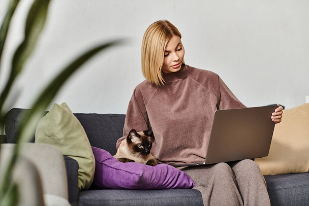 Kurzhaarige Frau genießt die Zeit zu Hause mit Laptop und Katze auf der Couch. - Foto, Bild