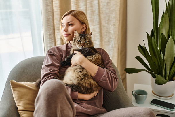 Krátkovlasá žena sedící na gauči, pokojně držící svou kočku v útulném vnitřním prostředí. - Fotografie, Obrázek