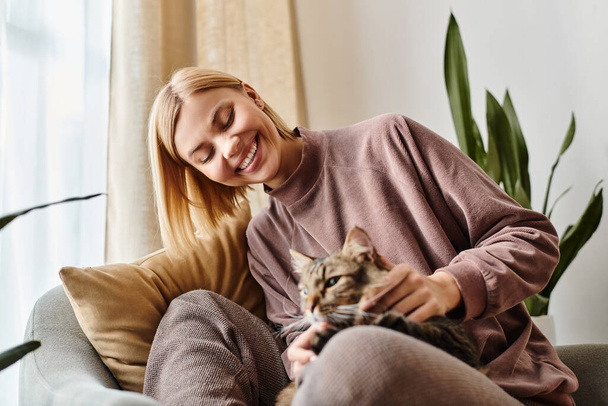 A stylish woman with short hair sitting on a couch, gently petting her content cat. - Photo, Image