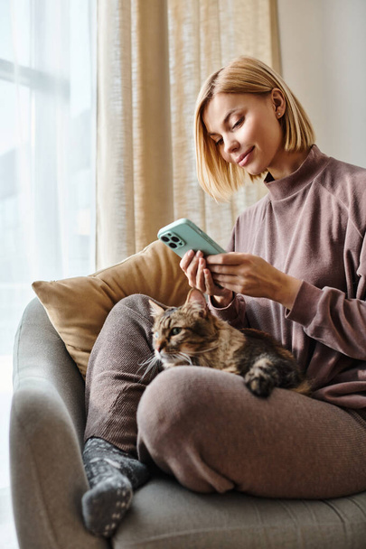 Una donna con i capelli corti che si rilassa su un divano mentre tiene affettuosamente il suo gatto. - Foto, immagini