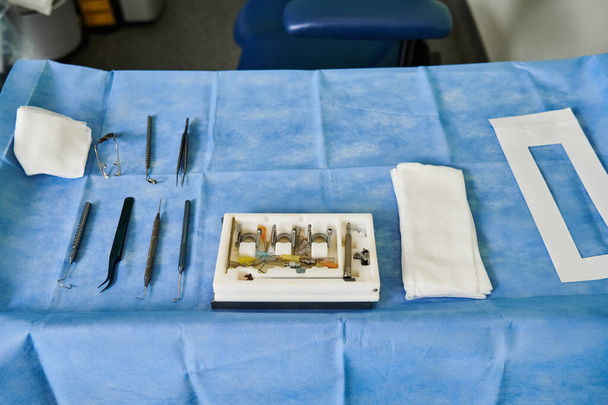 Ένα τραπέζι έχει στηθεί με χειρουργικό εξοπλισμό πάνω από ένα μπλε τραπεζομάντηλο. - Φωτογραφία, εικόνα
