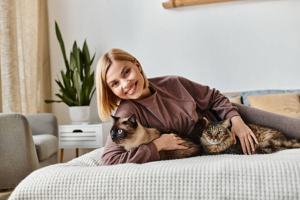 Eine Frau mit kurzen Haaren entspannt sich auf einem Bett und kuschelt in einem friedlichen Moment mit zwei Katzen zu Hause. - Foto, Bild