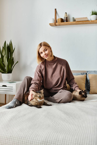 Une femme aux cheveux courts sereinement assise sur un lit, caressant doucement un chat calico à côté d'elle. - Photo, image