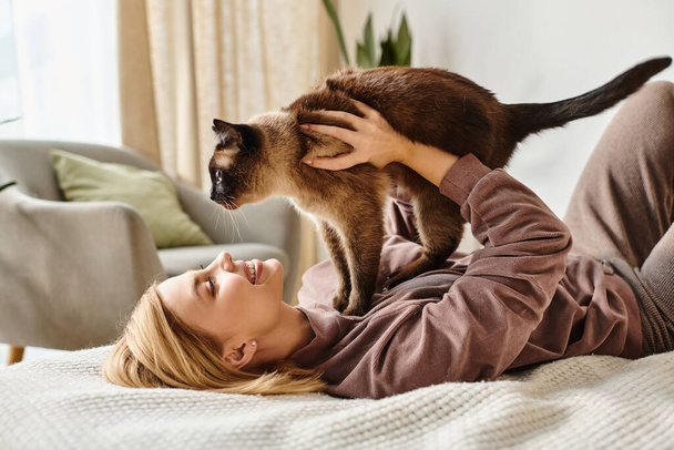 Een vrouw met kort haar ontspant zich op een bed, wiebelt haar kat in haar armen, ademt rust en tevredenheid uit. - Foto, afbeelding