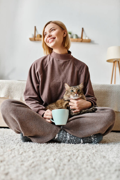Egy rövid hajú nő békésen ül a padlón, a macskáját a karjaiban tartva otthon.. - Fotó, kép