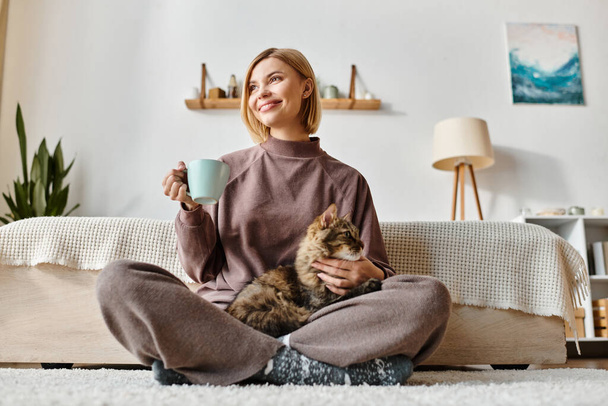 Nainen lyhyet hiukset istuu viihtyisä sohvalla, hymyillen, pitäen hänen suloinen kissa sylissään. - Valokuva, kuva