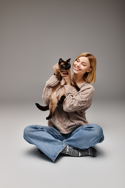 Eine Frau mit kurzen Haaren findet Frieden, während sie auf dem Boden sitzt und ihre geliebte Katze im Arm hält. - Foto, Bild