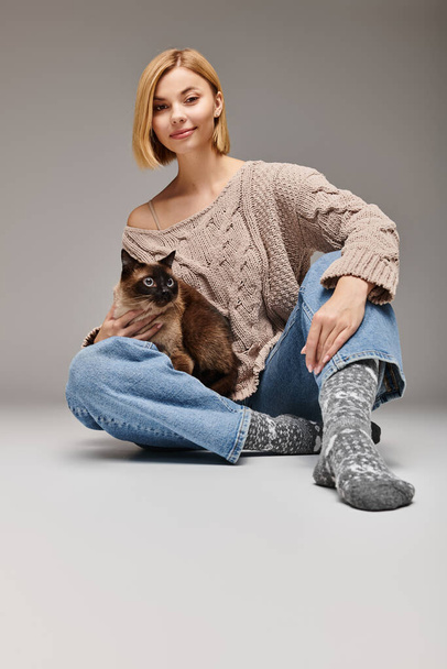 Kobieta z krótkimi włosami siedząca na podłodze, z miłością trzymająca kota, dzieląc chwilę połączenia w domu. - Zdjęcie, obraz