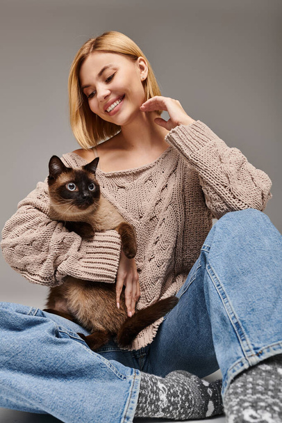 Kısa saçlı bir kadın yerde oturmuş kedisini sevgiyle tutuyor.. - Fotoğraf, Görsel