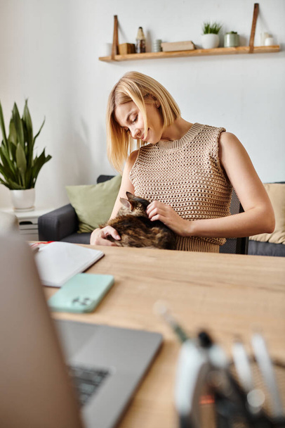 Nainen, jolla on lyhyet hiukset, istuu rauhallisesti pöydässä, silittää rakkaan kissansa varovasti kodikkaassa kotiympäristössä.. - Valokuva, kuva