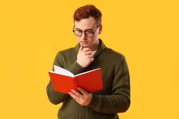 Junger Mann mit Brille liest Buch auf gelbem Hintergrund - Foto, Bild