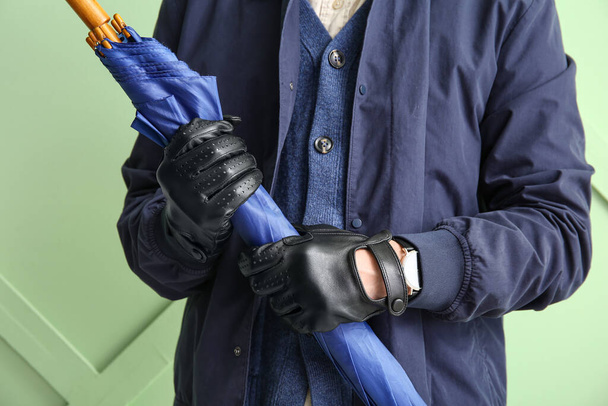 Man in stijlvol lederen handschoenen houden paraplu tegen kleur muur, close-up - Foto, afbeelding