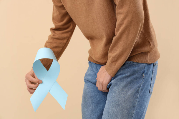 Joven con cinta azul sobre fondo beige, primer plano. Concepto de conciencia del cáncer de próstata - Foto, imagen