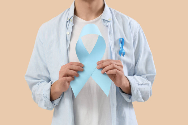 Joven con cintas azules sobre fondo beige, primer plano. Concepto de conciencia del cáncer de próstata - Foto, imagen