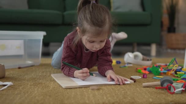 Une fille caucasienne tout-petit jouer sur le sol à la maison dessiner avec stylo - Séquence, vidéo