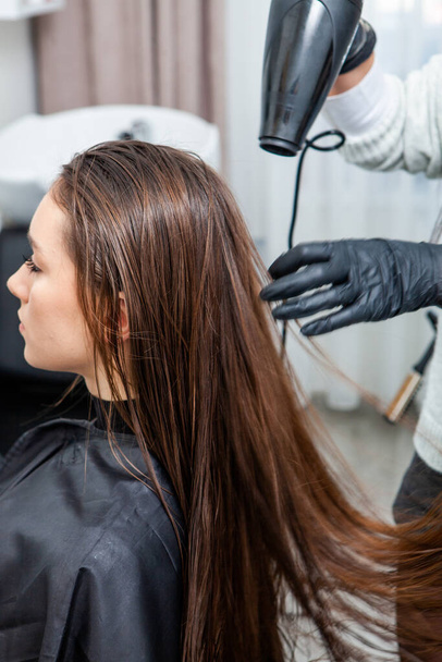 Foto eines europäischen Mädchens mit langen und schönen brünetten Haaren im Schönheitssalon. Glänzendes und gesundes Haar. - Foto, Bild