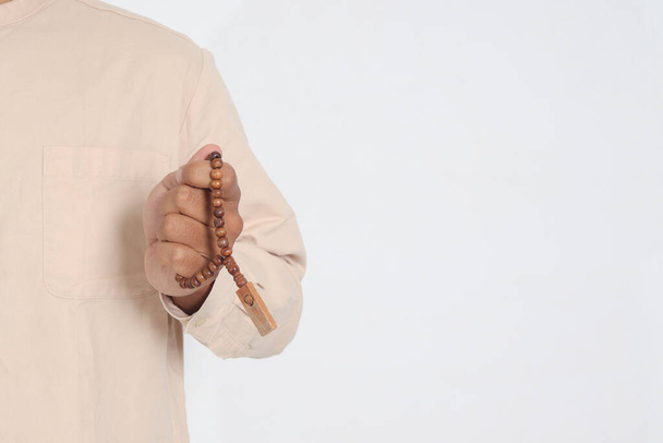 Zamknij rękę religijnego azjatyckiego muzułmanina w koko koszuli z czaszką modlącego się z podniesionymi rękami, trzymającego kulki islamskie. Pobożna koncepcja wiary. Izolowany obraz na białym tle - Zdjęcie, obraz