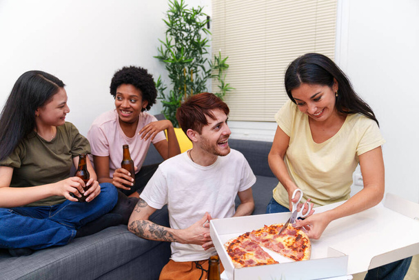 A barátok összegyűlnek a kanapén egy születésnapi ünnepségre, sörrel koccintanak és finom pizzát osztanak meg egy nyugodt lakásban.. - Fotó, kép