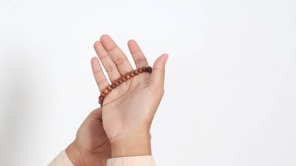 Zamknij rękę religijnego azjatyckiego muzułmanina w koko koszuli z czaszką modlącego się z podniesionymi rękami, trzymającego kulki islamskie. Pobożna koncepcja wiary. Izolowany obraz na białym tle - Zdjęcie, obraz