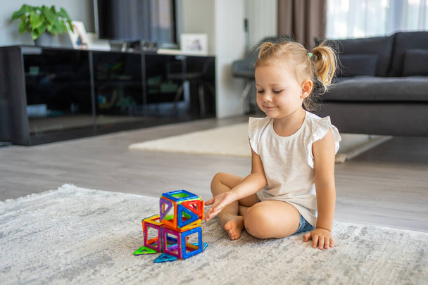 Little girl playing colorful magnet plastic blocks kit at home. The child playing educational games. Early childhood development. High quality photo - Photo, Image