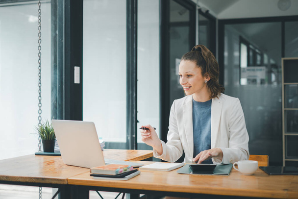 Концепція бізнес-аналізу, Контент-бізнес-леді займається своєю роботою на ноутбуці в сучасному офісному просторі, з чашкою кави під рукою - Фото, зображення