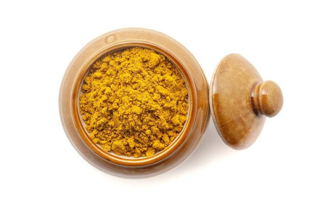 Vista superior del polvo digestivo orgánico llamado "Buknu" una mezcla de hierbas ayurvédicas indias y especias, en un frasco de cerámica. Aislado sobre un fondo blanco. - Foto, imagen