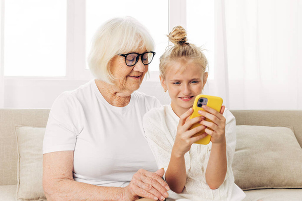 Селфи вызова копия единения улыбаясь космический телефон в помещении футболка диван ребенок воспитания бабушка семья связи видео счастье внучка белая обнимая фотография два - Фото, изображение