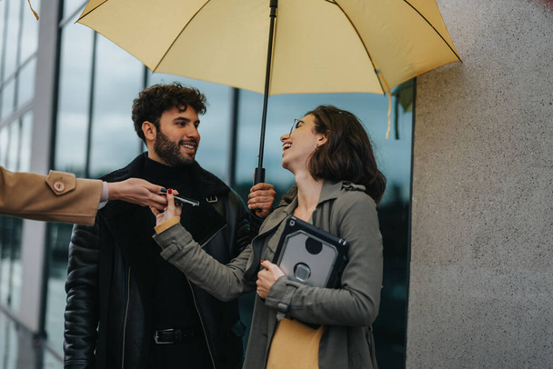 Amigos alegres compartiendo un paraguas amarillo en un día lluvioso de la ciudad. - Foto, Imagen