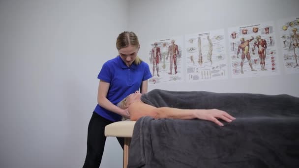 Сеанс натурального масажу, терапевт масажує м'язи шиї літньої жінки. Жіночий масажист робить терапевтичний масаж шиї для жінки, що лежить на дивані в красивому спа-центрі.  - Кадри, відео