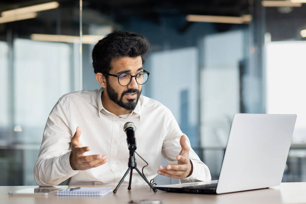 Уверенный индиец с бородой проводит деловую встречу по видеосвязи на ноутбуке в хорошо освещенном офисе. - Фото, изображение