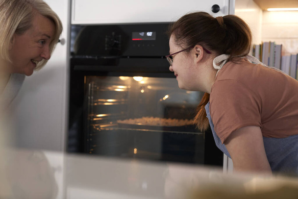 Down-szindrómás nő és az anyja házi készítésű sütikre várnak a sütőben. - Fotó, kép