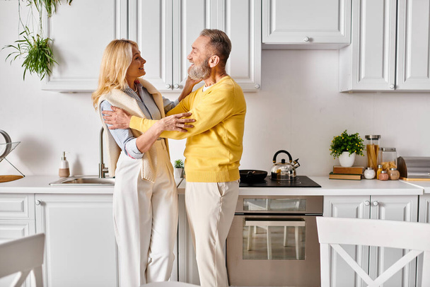 Ώριμος άντρας και γυναίκα με ζεστά ρούχα στο σπίτι, με αγάπη περνούν χρόνο μαζί στην κουζίνα στο σπίτι. - Φωτογραφία, εικόνα
