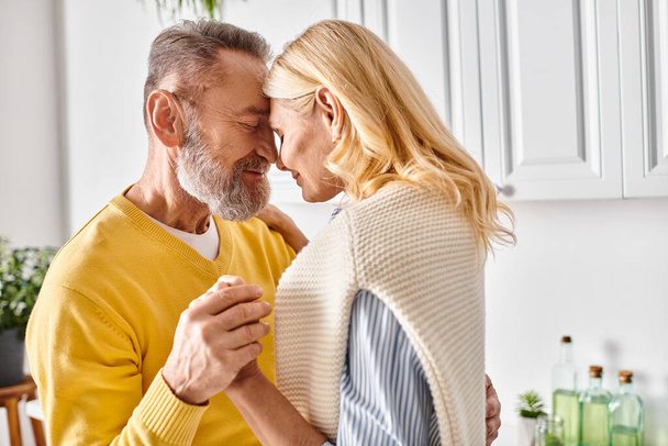 Un couple aimant mature dans des vêtements confortables embrasser dans leur cuisine, partageant un moment de convivialité. - Photo, image