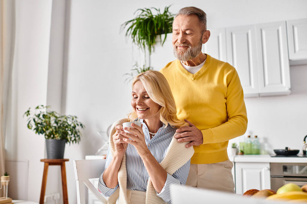 A mature loving couple in cozy homewear stands side by side in a kitchen, sharing a moment of togetherness. - Photo, Image