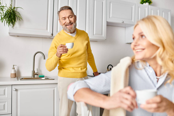 Зрелая любящая пара в уютной домашней одежде проводит время вместе на теплой и уютной кухне. - Фото, изображение