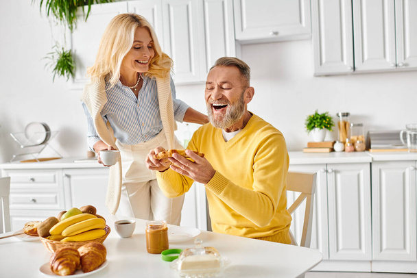 Dojrzały mężczyzna i kobieta ubrani w przytulne homewear siedzi przy stole w kuchni, ciesząc się chwilą razem w domu. - Zdjęcie, obraz