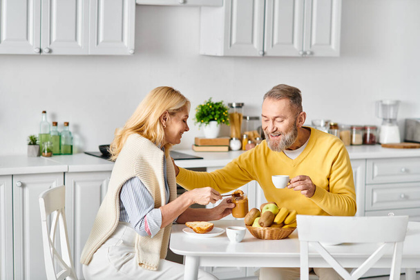 Ein reifes, liebevolles Paar in gemütlicher Hauskleidung genießt eine gemeinsame Mahlzeit an einem Tisch in seinem Haus. - Foto, Bild