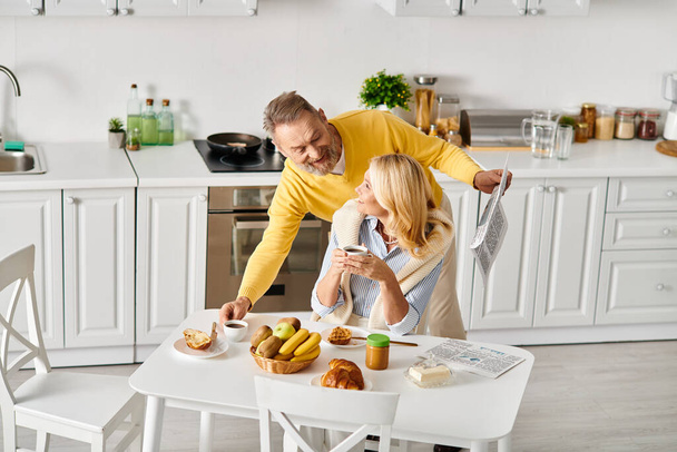 Egy érett férfi és a felesége együtt pózolnak egy hangulatos konyhában, megosztva egy szerető és szívből jövő pillanatot.. - Fotó, kép