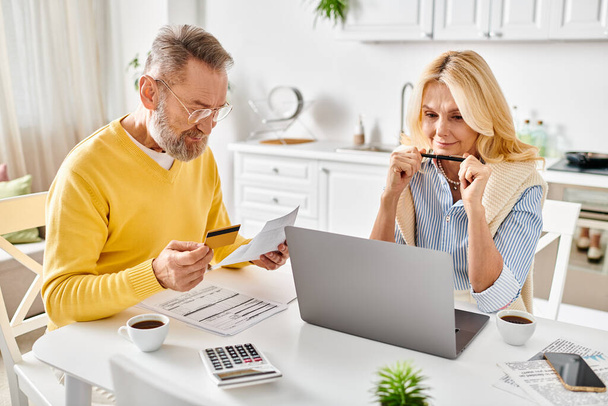 A mature couple in cozy homewear deeply engrossed in reviewing paperwork together at a table in their kitchen. - Photo, Image