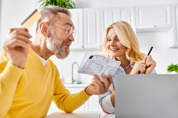 A mature loving couple in cozy homewear examining a piece of paper together in their kitchen at home. - Photo, Image