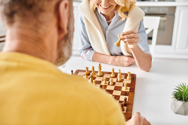 Ein reifes Liebespaar in gemütlicher Hausmannskleidung sitzt einander gegenüber, zutiefst konzentriert, während sie zu Hause eine Partie Schach spielen.. - Foto, Bild