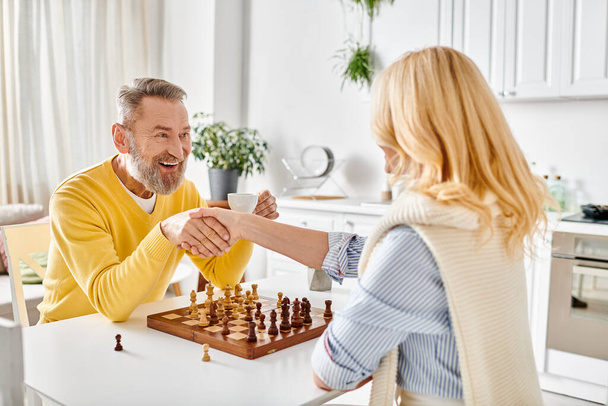 Egy érett férfi és nő részt vesz egy stratégiai játék a sakk a hangulatos konyhában, élvezi egy pillanatra az intellektuális kihívás és a kapcsolat. - Fotó, kép