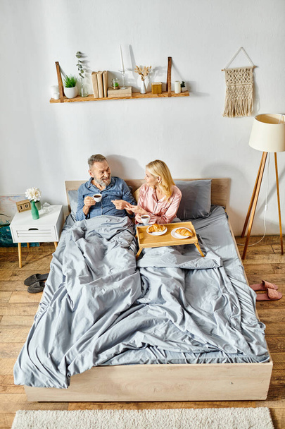 Egy érett szerető pár kényelmes otthonban, szorosan együtt ülnek az ágyon, egy békés és gyengéd pillanaton osztoznak.. - Fotó, kép